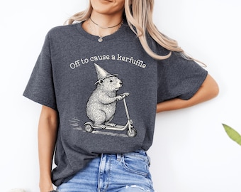 May include: Dark gray t-shirt with the phrase "Off to cause a kerfuffle" above a graphic of a rodent wearing a wizard hat and riding a scooter. The graphic is in black and white.