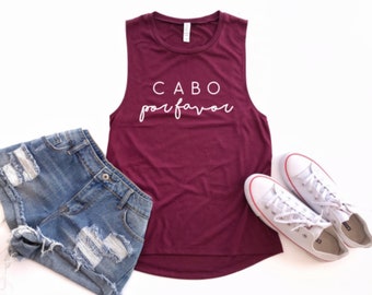 May include: A maroon sleeveless tank top with the text "CABO por favor" in white lettering. The tank top is paired with denim shorts and white sneakers.