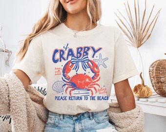 May include: Cream-colored t-shirt with a red and blue crab graphic. The graphic includes the text "If Crabby" and "Please Return to the Beach". A starfish and seashell are also included in the design.