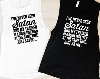 May include: Two sleeveless shirts with a white and black design. The text on the shirts reads "I've never seen Satan and my trainer in a room together at the same time. Just sayin'...".