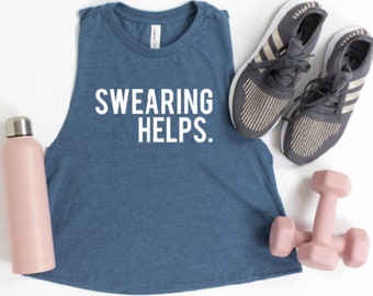 May include: A blue cropped tank top with the text "SWEARING HELPS." printed in white. The tank top is laying on a white surface with a water bottle, dumbbells, and a pair of gray running shoes.