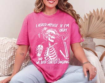 May include: A hot pink t-shirt with a white graphic of a skeleton wearing sunglasses, holding a drink, and the text "I asked myself if I'm okay...and we both started laughing."