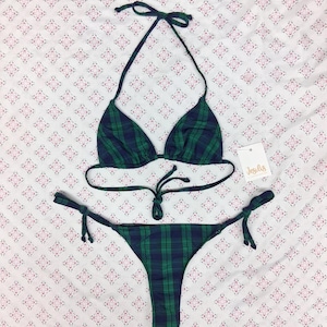 May include: A two-piece bikini set featuring a dark green and navy blue plaid pattern. The top has triangle cups with adjustable halter neck and back ties. The bottom is a classic cut with side tie closures. A small white tag reads Jesilus.