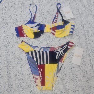 May include: A two-piece bikini set featuring a multicolored patchwork pattern with yellow, blue, red, and white sections. The top has an underwire design with thin straps, and the bottom is a high-cut style. Both pieces include white Jesilis tags.