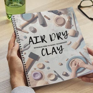 Puede incluir: Un libro encuadernado en espiral titulado "AIR DRY CLAY: Introduction to Basic Techniques" se sostiene abierto, mostrando ilustraciones de herramientas y proyectos de arcilla. La portada presenta un esquema de color azul claro y blanco, con el título en negrita negra.