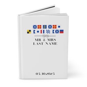 May include: White wedding guest book with a nautical theme. The cover features a string of nautical flags with the text "MR & MRS LAST NAME" and the date "05.30.2025".