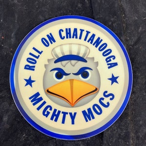 May include: A blue and white round sticker with the words "Roll on Chattanooga Mighty Mocs" and a cartoon mascot with a blue hat and a yellow beak.