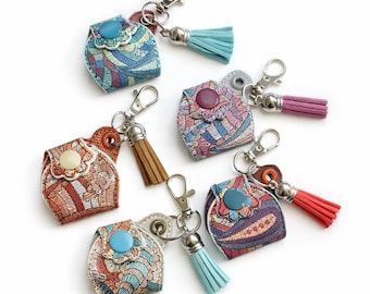 Puede incluir: Una colección de llaveros coloridos y estampados con pequeñas bolsas y borlas. Cada llavero presenta una combinación de colores única, que incluye azul, naranja y morado, con un cierre plateado. Las borlas vienen en varios colores.
