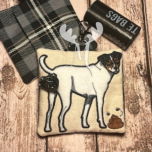May include: A white and black dog with a brown poop emoji embroidered on a beige fabric pouch. The pouch has a black and white plaid fabric on the back. The pouch is attached to a black roll of "P.T.E. BAGS" dog waste bags.