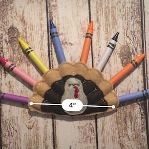 Puede incluir: Un porta l&aacute;pices de fieltro con forma de pavo con un cuerpo marr&oacute;n, plumas negras y una barbilla roja. El porta l&aacute;pices tiene 10 cm de ancho y tiene ocho l&aacute;pices que sobresalen. Los l&aacute;pices son morado, azul, blanco, naranja, amarillo, rosa y rojo.