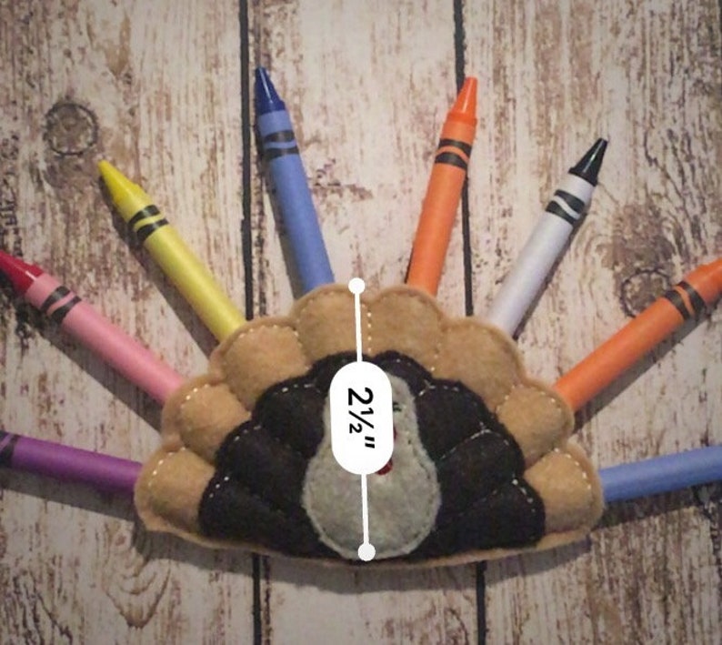 Puede incluir: Una manualidad de pavo de fieltro con un cuerpo marr&oacute;n y plumas negras. El pavo tiene una cabeza gris y un pico rojo. El pavo mide 2 1/2 pulgadas de alto. El pavo est&aacute; rodeado de crayones de varios colores.