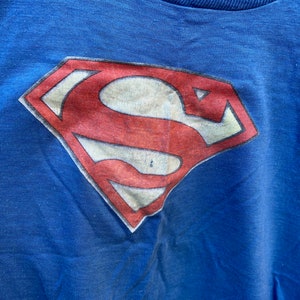 May include: A blue t-shirt with a red and white Superman logo printed on the front.