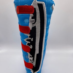 May include: A blue quilted golf club head cover with a black and white embroidered ship design and red stripes.