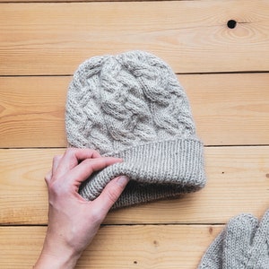 May include: A pair of gray knitted mittens and a matching gray knitted hat. The hat has a cable knit pattern and the mittens have a similar pattern.