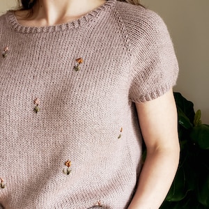 Peut inclure: Un pull en maille mauve à manches courtes et fleurs brodées. Le pull est fait d'un fil doux et léger et a une coupe décontractée.