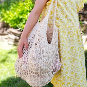 May include: A cream-colored, open-weave net bag filled with yarn. The bag is carried by a person wearing a yellow floral dress. The bag's design is reminiscent of a market bag, suitable for carrying groceries or craft supplies.