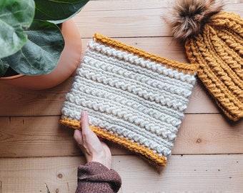 May include: A white knitted infinity scarf with a yellow crocheted border. The scarf is being held by a hand.