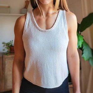 May include: A white knitted tank top with a scoop neck. The tank top is made from a soft, lightweight fabric and has a relaxed fit.