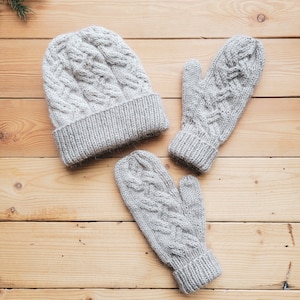 May include: A set of grey knitted winter accessories, including a hat and mittens. The hat and mittens have a cable knit pattern.