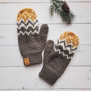 Puede incluir: Un par de guantes de punto marrones con un patrón geométrico blanco y amarillo. Los guantes tienen una etiqueta de cuero con un pequeño diseño de árbol.