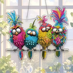May include: A colorful bird-themed wall hanging featuring four cartoon birds perched on a branch. The birds have large eyes and vibrant plumage in shades of pink, blue, yellow, and green. The artwork is suspended by a silver chain, creating a whimsical decorative piece.