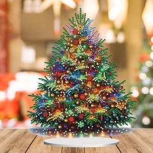 May include: A decorative tabletop Christmas tree featuring a dense arrangement of green pine needles adorned with numerous multi-colored, reflective, and faceted circular ornaments in shades of red, blue, gold, and purple, set on a circular base.