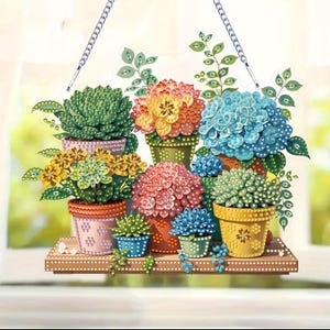 May include: A decorative hanging sign featuring colorful potted succulents and flowers. The sign has a wooden shelf design with various sizes and colors of plants, including green, yellow, orange, pink, and blue. A silver chain is attached for hanging.