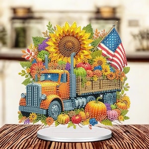 May include: A yellow truck with a wooden bed filled with pumpkins, apples, and sunflowers. The truck is surrounded by fall foliage and an American flag.