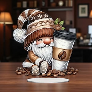 Könnte beinhalten: Eine skurrile Zwergenfigur mit weißem Bart, braunem Hut und Jacke, die eine Kaffeetasse hält. Die Tasse hat eine Kaffeebohnen-Grafik. Kaffeebohnen umgeben den Zwerg, und ein weißer Untersetzer ist davor.
