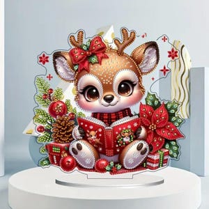 May include: A decorative Christmas-themed figurine of a cartoon deer reading a book. The deer has brown fur with white spots, large eyes, and a red bow. It is surrounded by Christmas decorations, including a poinsettia and presents.