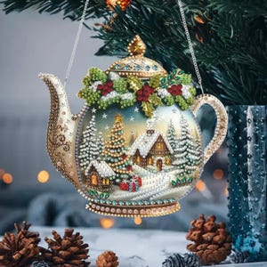 May include: A teapot-shaped Christmas ornament featuring a beaded winter scene with a snow-covered cabin, a decorated pine tree, and presents. The lid is adorned with holly leaves and red berries, while the entire surface is covered in sparkling beads.