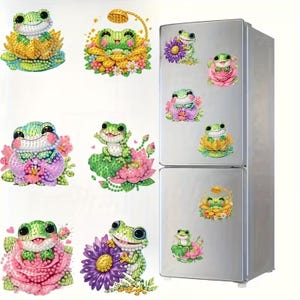 May include: A collection of diamond painting stickers featuring green frogs sitting on various colorful flowers including pink roses, purple daisies, and yellow lotus blossoms. Some frogs are shown with small shower heads above their heads.