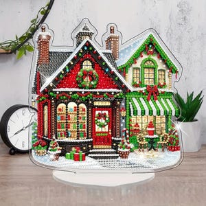 May include: A decorative tabletop display featuring a diamond art bookshop building with a red and green facade, snow-covered roof, and festive wreaths. The structure includes a storefront window, a door labeled BOOKSHOP, and small gift boxes.