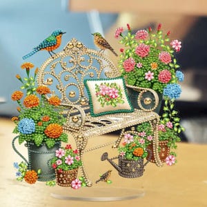 May include: A decorative garden scene featuring a gold-colored bench adorned with flowers and two birds. The bench has a small pillow with a floral design. Potted flowers in shades of orange, pink, and blue surround the bench, creating a vibrant display.