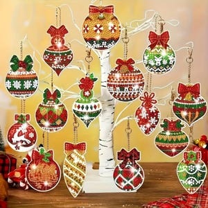 Op de afbeelding: Een verzameling kerstversieringen in verschillende vormen, waaronder ronde en druppelvormige ontwerpen. De ornamenten zijn versierd met rode, groene en gouden patronen, strikken en hangende kettingen. Ze worden tentoongesteld op een witte decoratieve boom.