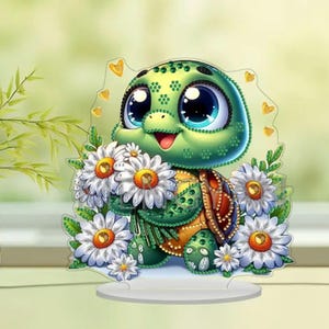 May include: A whimsical, green turtle figurine with large blue eyes, holding a bouquet of white daisies with yellow centers. The turtle has a brown shell and is set on a white base. Decorative hearts surround the turtle.