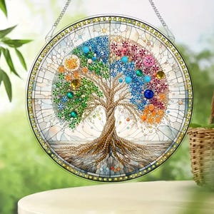 May include: A round stained glass window featuring a tree design. The tree has a brown trunk and roots, with colorful leaves and accents in shades of green, blue, pink, and orange. The window is framed with a gold border and a chain for hanging.