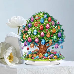 May include: A colorful Easter tree decoration featuring a brown trunk, green leaves, and numerous decorated Easter eggs in various colors. The tree sits on a clear stand, with additional eggs at the base. White flowers are also present.
