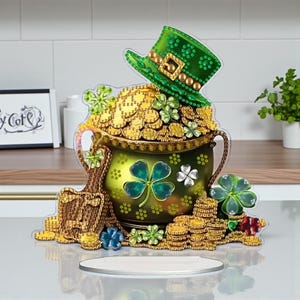 May include: A St. Patrick's Day decoration featuring a green pot of gold overflowing with coins, a green leprechaun hat, and shamrocks. The pot is decorated with a four-leaf clover design. The base is a silver-colored oval.