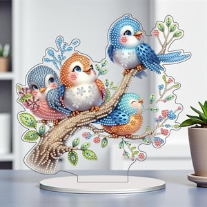 May include: A decorative acrylic bird scene featuring four colorful birds perched on a branch. The birds have blue, orange, and pink feathers, with a white base. The branch has green leaves and pink and blue flowers.