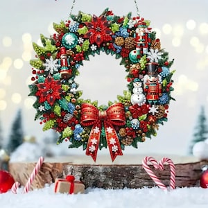 May include: A circular Christmas wreath decorated with red poinsettias, green holly leaves, red berries, pinecones, and blue accents. The wreath features two nutcracker figures, a small snowman, and a large red bow with white snowflake patterns.