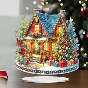 Puede incluir: Una pintura de diamantes 3D que representa una casa de Navidad con una ventana iluminada y un árbol de Navidad decorado con adornos. La casa está rodeada de nieve y regalos.