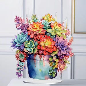 May include: A vibrant, layered succulent arrangement in a blue pot. The artwork features a variety of succulents in shades of red, orange, yellow, green, and purple. The pot has a watercolor effect and sits on a clear base.