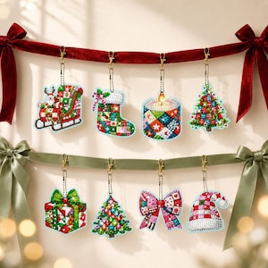 Puede incluir: Ocho adornos de pintura de diamantes colgados de dos cintas. Los adornos muestran un trineo de Santa, un calcetín, una vela, un árbol de Navidad, un regalo, otro árbol, un lazo y un gorro de Santa, decorados con un diseño de mosaico multicolor.