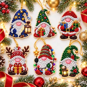 May include: Six diamond painting Christmas ornaments featuring gnomes and Santa Claus. Each wooden cutout is decorated with colorful faceted beads and pearls, depicting festive characters with hats, lanterns, gifts, and reindeer antlers, all suspended by gold strings.