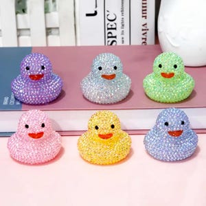 Peut inclure: Six figurines de canard ornées de cristaux dans différentes couleurs : violet, argent, vert, rose, jaune et bleu. Chaque canard a un bec rouge et des yeux noirs. Les canards sont recouverts de cristaux étincelants.
