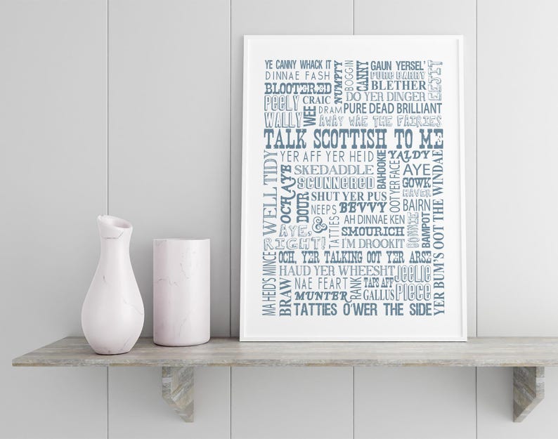 May include: A white framed wall art print featuring a collection of Scottish slang words and phrases in various blue fonts, including the central text TALK SCOTTISH TO ME, displayed alongside a white marble vase and a cylindrical white container.