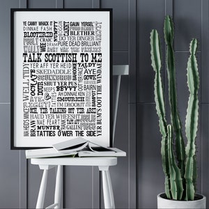 May include: A black framed wall art print featuring a collection of Scottish slang words and phrases in various black fonts on a white background, with the central text reading TALK SCOTTISH TO ME, displayed in a vertical rectangular orientation.