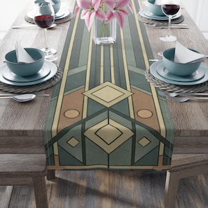 May include: An Art Deco style table runner in green, tan, and cream. The geometric design features diamonds, ovals, and vertical stripes. The runner is set on a wooden table with teal bowls, plates, and wine glasses. The table is set for a meal.