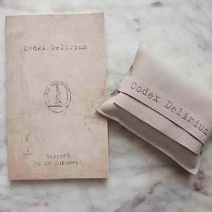 Peut inclure: Un livre d'aspect vieilli et une petite pochette, tous deux portant l'inscription "Codex Delirium". Le livre présente un aspect délavé avec un tampon et le texte "Rapport du Dr Zubovski". La pochette est beige clair avec une lanière assortie.